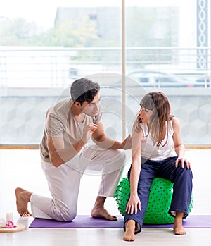 Personal coach helping woman in gym with stability ball