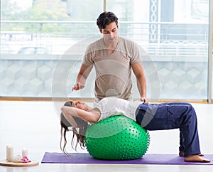 Personal coach helping woman in gym with stability ball