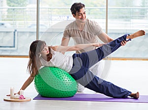 Personal coach helping woman in gym with stability ball