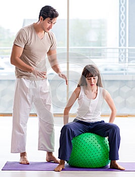 Personal coach helping woman in gym with stability ball