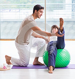 Personal coach helping woman in gym with stability ball