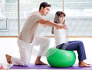 Personal coach helping woman in gym with stability ball