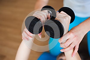 Personal coach helping woman to do exercises with dumbbells in gym
