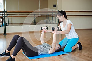 Personal coach helping woman to do exercises with dumbbells in gym.