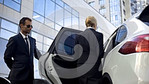 Personal driver waiting for boss on parking lot, helping her to get into car