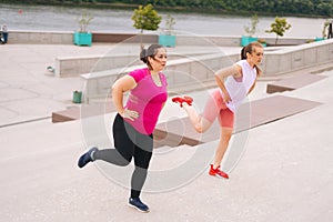 Personal fitness female trainer helping fat woman lose weight outside taking step exercising on city stairs in summer