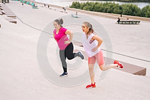 Personal fitness female trainer helping fat woman lose weight outside taking step exercising on city stairs in summer
