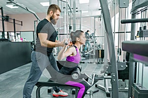 Personal fitness trainer coaching and helping client woman making exercise in gym. Sport, teamwork, training, people concept