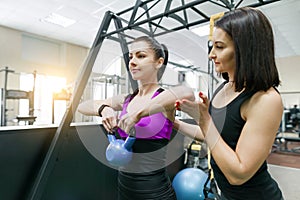 Personal fitness trainer coaching and helping client woman making exercise with weight in gym. Fitness, sport, training, people,