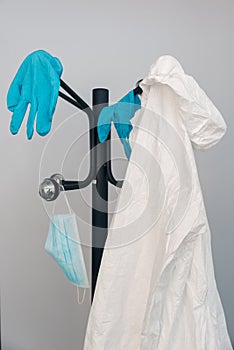 Personal protective equipment white NBC suit, surgical face mask and blue nitrile gloves hanging on a hanger, against covid-10