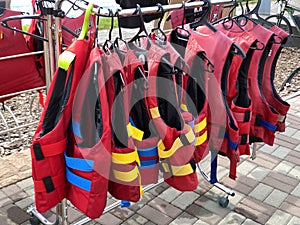 Personal red life vests in store. Many life jackets hang in a row on hangers. Protective safety clothing at rental boat store or