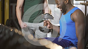 Personal trainer actively motivating young man during dumbbell exercise in gym