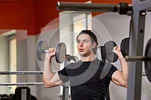 Personal Trainer in black t-shirt doing sitting dumbbell curls for training his biceps, in a gym