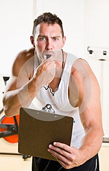 Personal trainer blowing whistle in health club