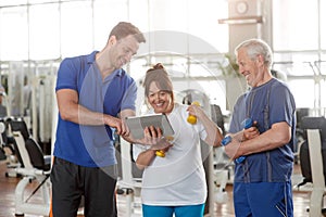 Personal trainer giving instructions to elderly couple in gym.