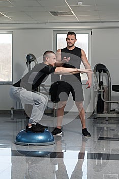 Personal Trainer Helping Man On Bosu Balance Ball
