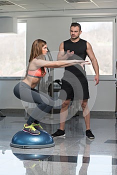 Personal Trainer Helping Woman On Bosu Balance Ball