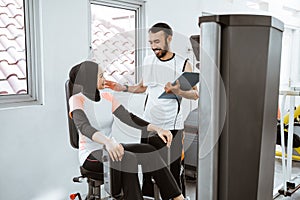 Personal trainer helping woman working with leg weight machine at the gym