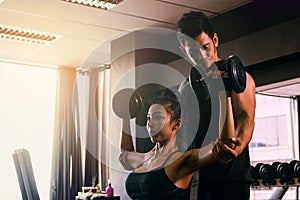 Personal trainer helping woman working lift heavy dumbbells two