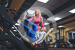 Personal trainer helping woman in works out on training apparatus inside in fitness center. Sporty lifestyle