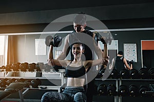 Personal trainer helping woman working lift heavy dumbbells two