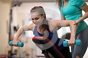 Personal trainer helping young woman with weight training equipment in gym photo