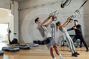 Personal trainer helps a couple that work out with elastic resistant strap.