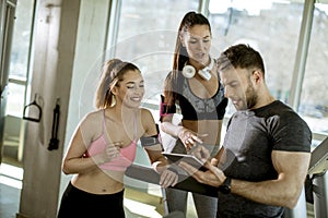 Personal trainer looking at digital tablet and explaining progress to young women at the gym