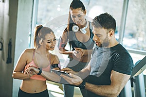 Personal trainer looking at digital tablet and explaining progress to young women at the gym