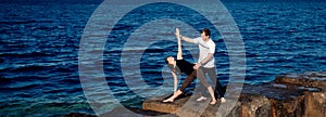 Personal trainer man correct woman client while doing stretching or yoga outdoors background sea. Concept banner asana