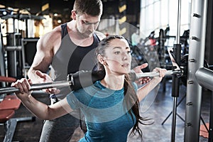 Personal trainer man helps woman work with barbell at squat exercises in gym