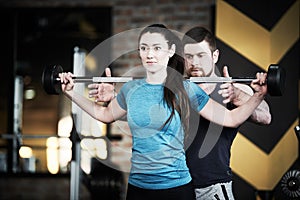 Personal trainer man helps woman work with barbell at squat exercises in gym