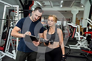 personal trainer with slim woman client doing bicep curls working out in gym