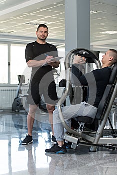 Personal Trainer Takes Notes While Man Exercising Chest