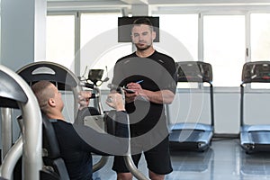 Personal Trainer Takes Notes While Man Exercising Chest