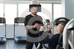 Personal Trainer Takes Notes While Man Exercising Chest