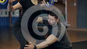 Personal trainer teaches girl to do an exercise with barbell on her shoulders.