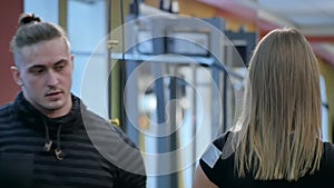 Personal trainer watching young woman using barbells in the gym