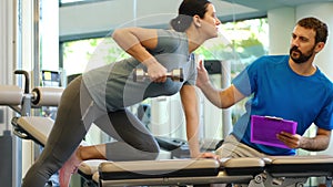 Personal trainer working with client in gym. Trainer man helping young woman with her work out with dumbbells