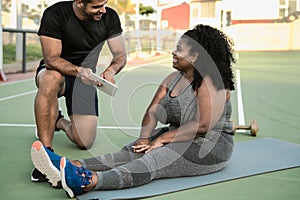 Personal trainer working with curvy woman while giving her istruction with digital tablet during training session