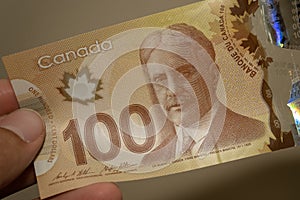 Persons hand giving the Currency of the Canada - One brown hundred dollar notes spread out on a brown background. Money exchange