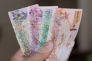 Persons hand giving the Currency of the Qatar - hundreds of rial or riyal notes spread out on a brown background. Money exchange