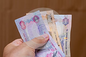Persons hand giving the Currency of the United Arab Emirates UAE - Multiple hundred Dirham notes spread out on a brown