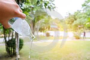 Persons hand holding a bottle of water poring it out in garden,