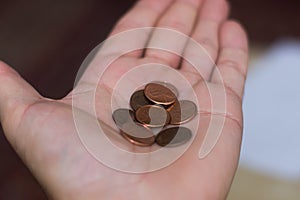 Persons hand holding out a a handful of United States of America USA pennies, a useless coin on a brown background. Money photo