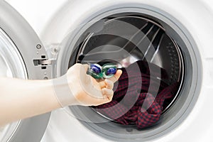 persons hand put special cleaning pod or capsule in the washing machine with dirty cloth