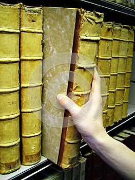 Persons hand removing old book from bookshelf