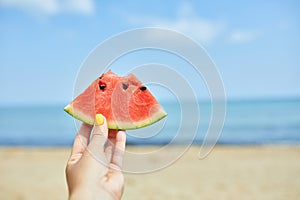 Hand Holding a Slice of Watermelon on a Sunny Beach Day