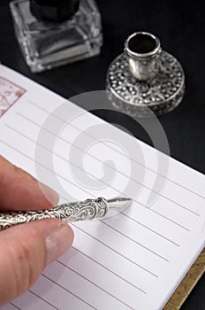 Persons Hand Writing with a Metal Fountain Pen with Gall Bottle and Pen Holder on Dark Background