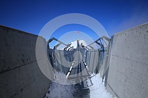 Perspctive view on Steel hanging bridge between ice mountain peak middle blue clear sky background and white cloudy on winter